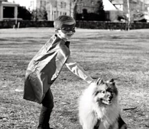 Boy wearing Captain Pawsitive cape, petting dog