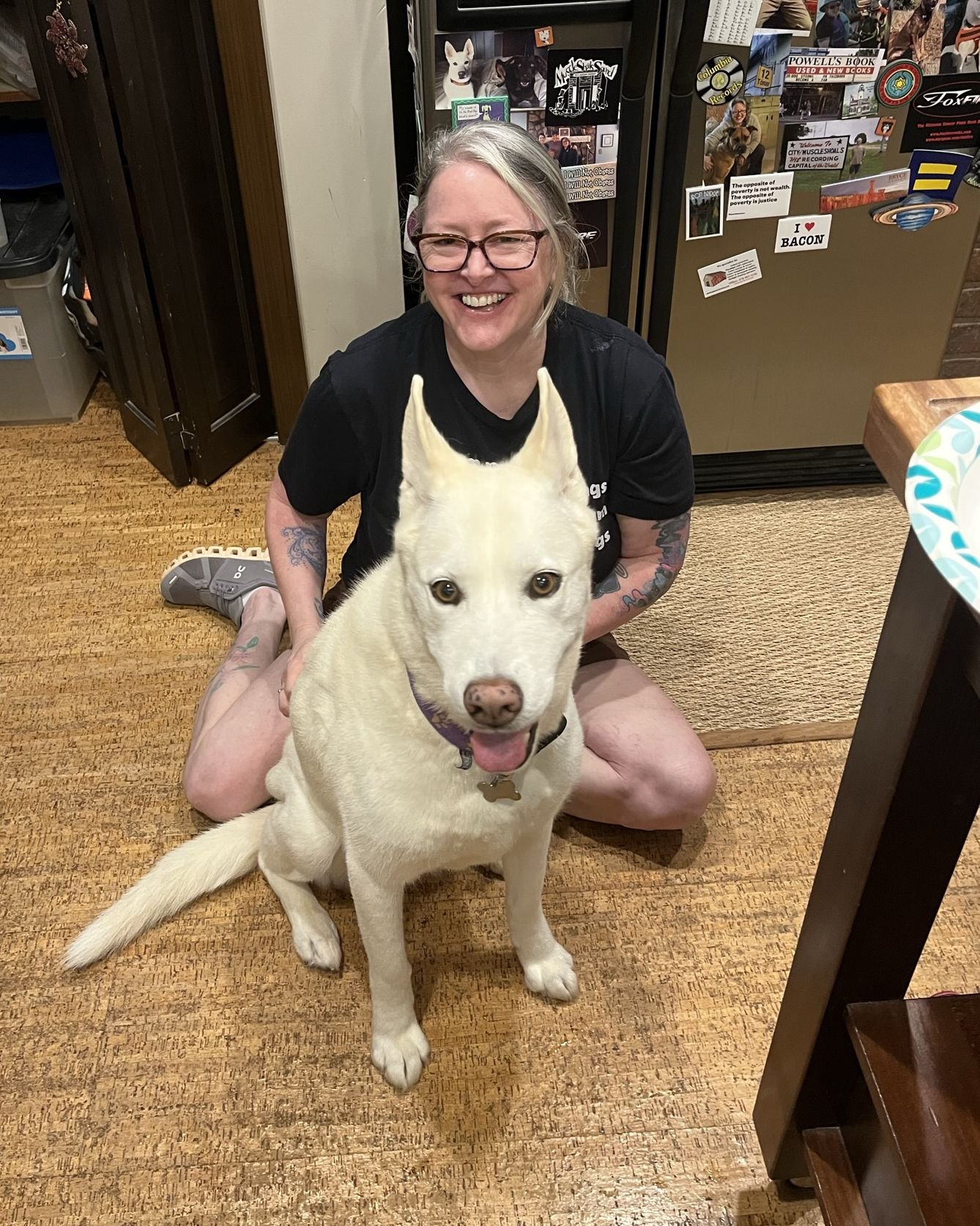 A woman sitting on the floor smiling with a large white dog sitting in front of her.